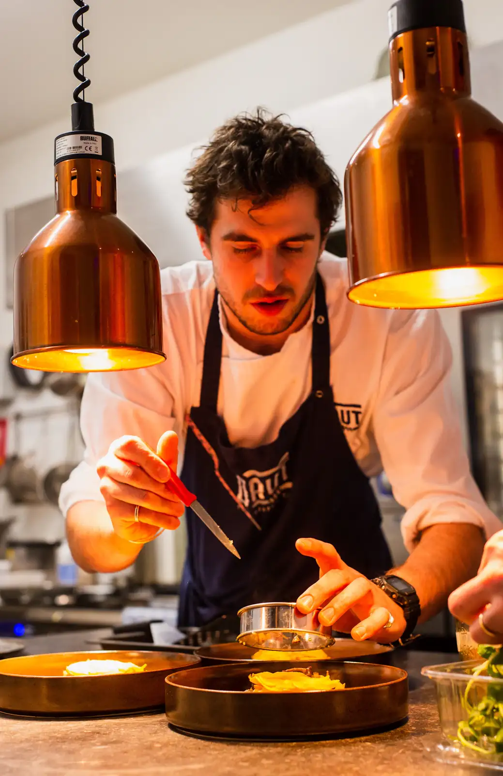 Chef dressant une assiette sous des lampes en cuivre